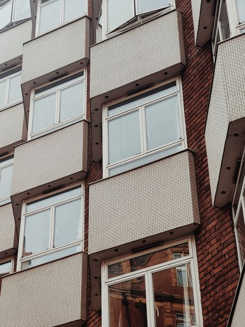 A close-up view of the exterior façade of an existing residential building, featuring multiple white-framed double-glazed windows set into brickwork and textured paneling. The building's corner secti